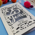 25th Anniversary Card with '25 Years' and 'Kelly and Ryan' text on a blue background with colourful pom-poms.