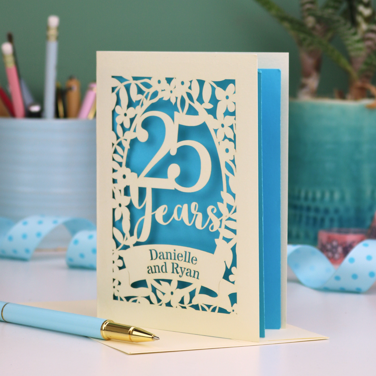 Silver anniversary Card with '25 Years' and 'Danielle and Ryan' on a desk with stationery items.