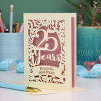 25th anniversary Card with '25 Years' and 'Danielle and Ryan' on a desk with stationery items.