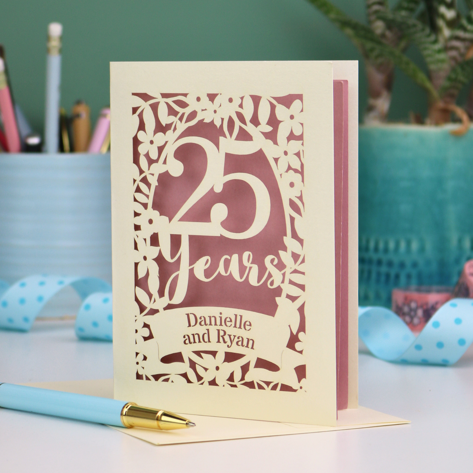 25th anniversary Card with '25 Years' and 'Danielle and Ryan' on a desk with stationery items.