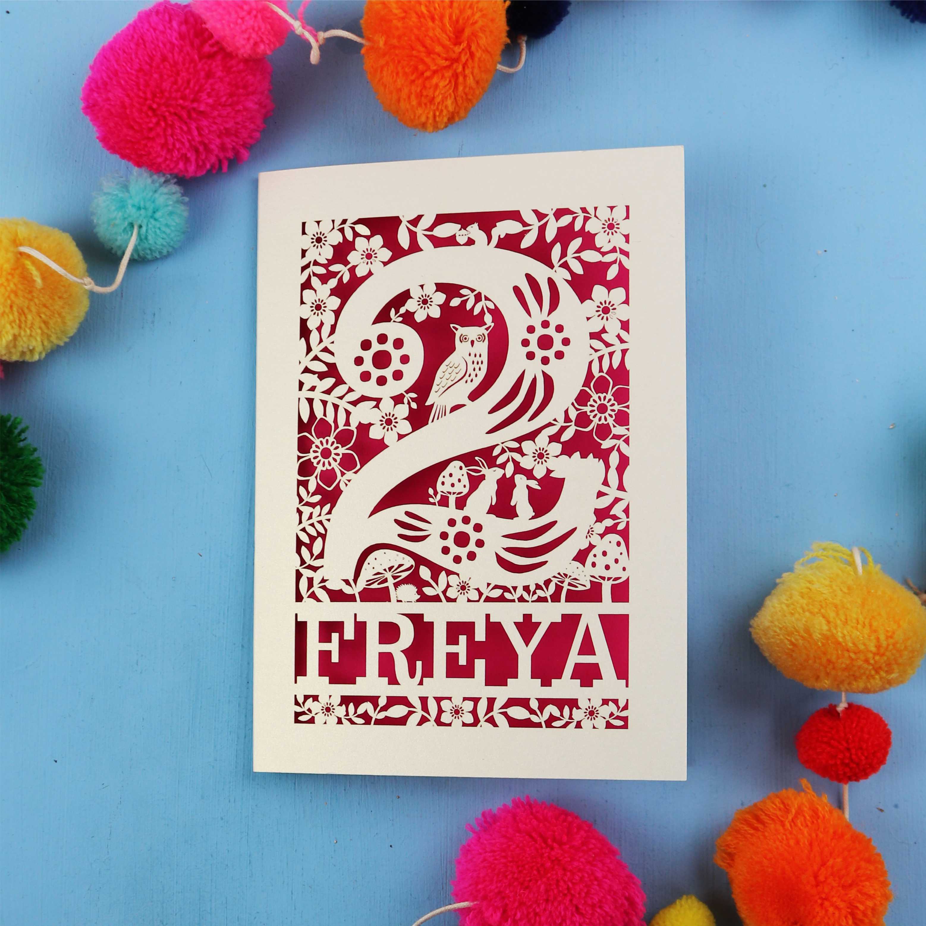 Decorative 2nd birthday card with 'FREYA' design on a blue background with colourful pom-poms.