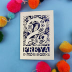 Laser cut 2nd birthday card with woodland design on a blue background with colourful pom-poms.