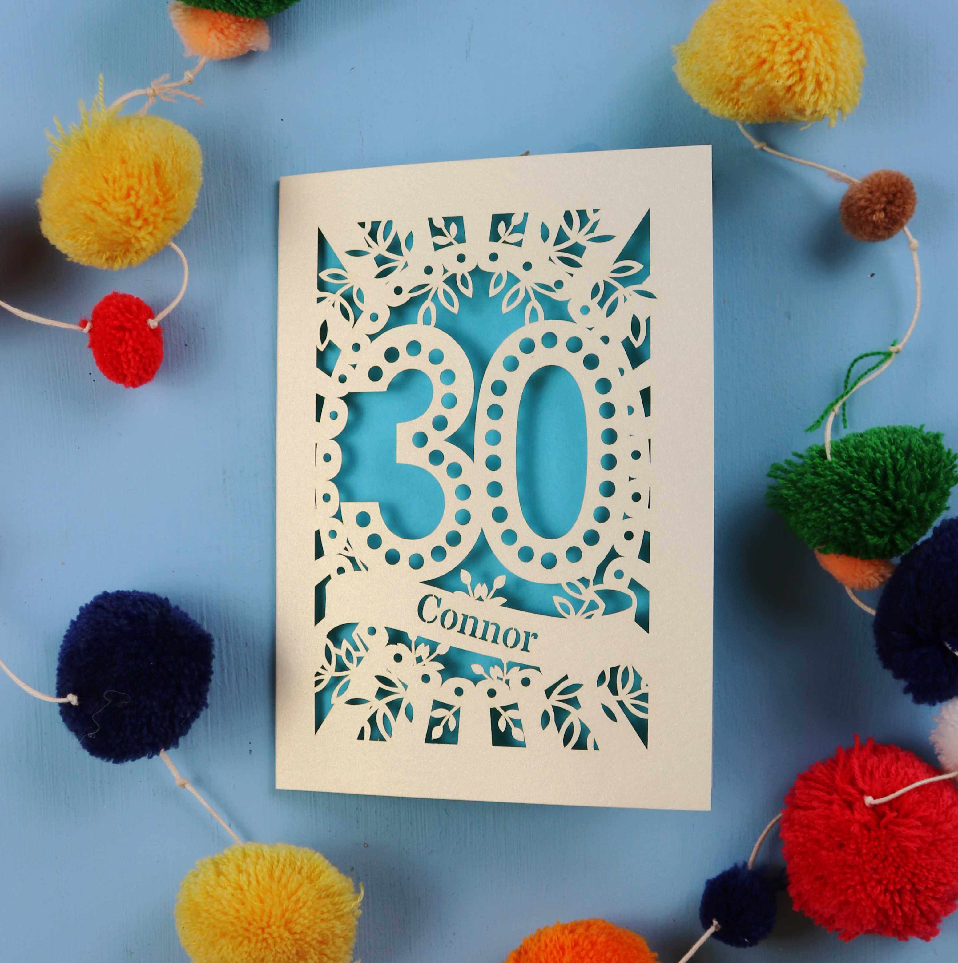 Laser cut 30th birthday card with '30 Connor' on a blue background with colourful pom-poms