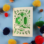 Laser cut 30th birthday card with '30 Connor' on a blue background with colourful pom-poms