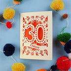 Laser cut 30th birthday card with '30 Connor' on a blue background with colourful pom-poms