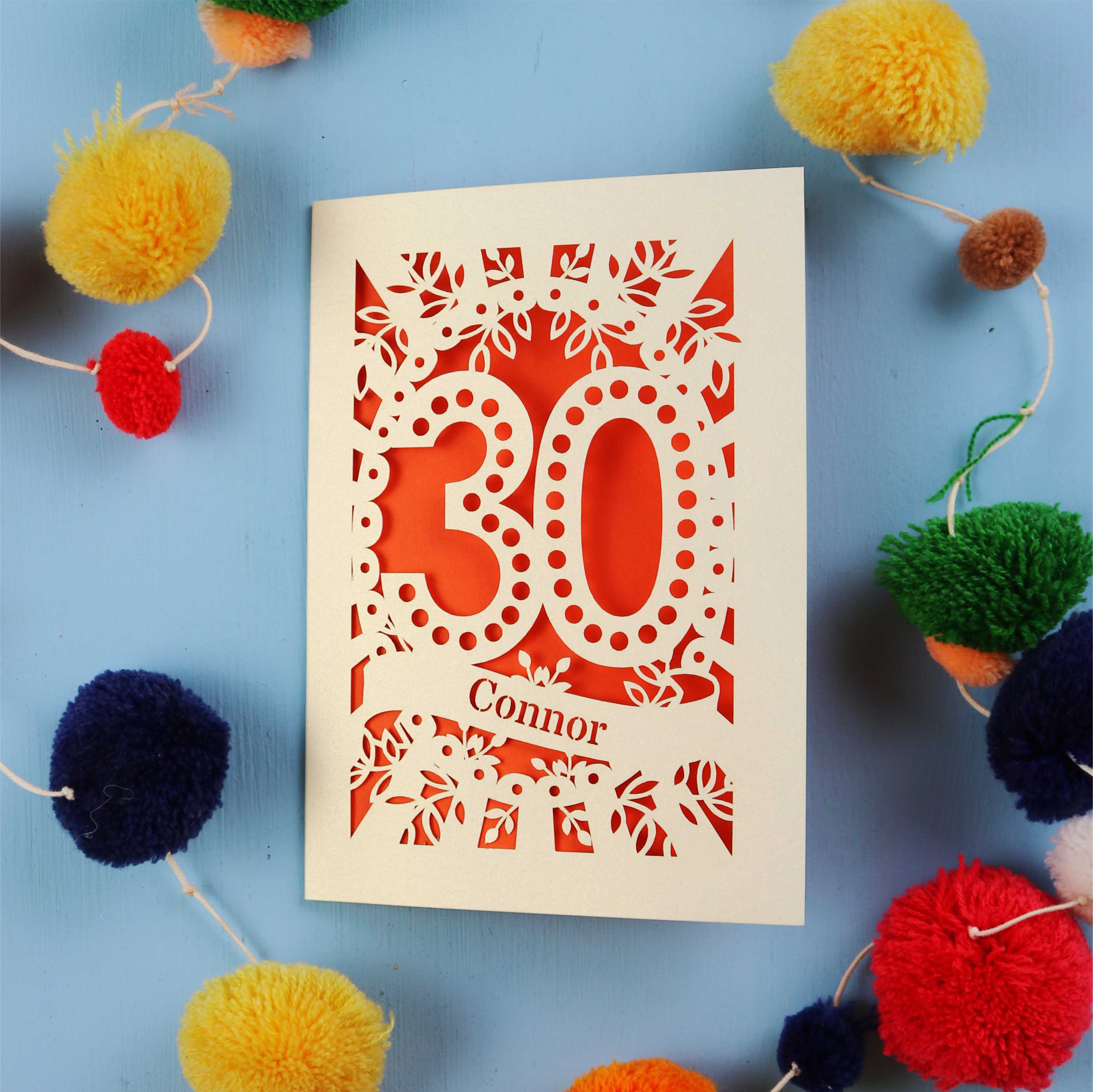 Laser cut 30th birthday card with '30 Connor' on a blue background with colourful pom-poms