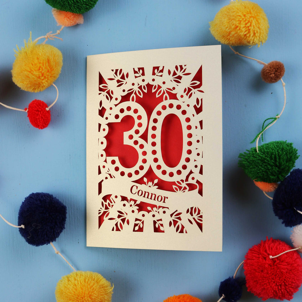 Laser cut 30th birthday card with '30 Connor' on a blue background with colourful pom-poms
