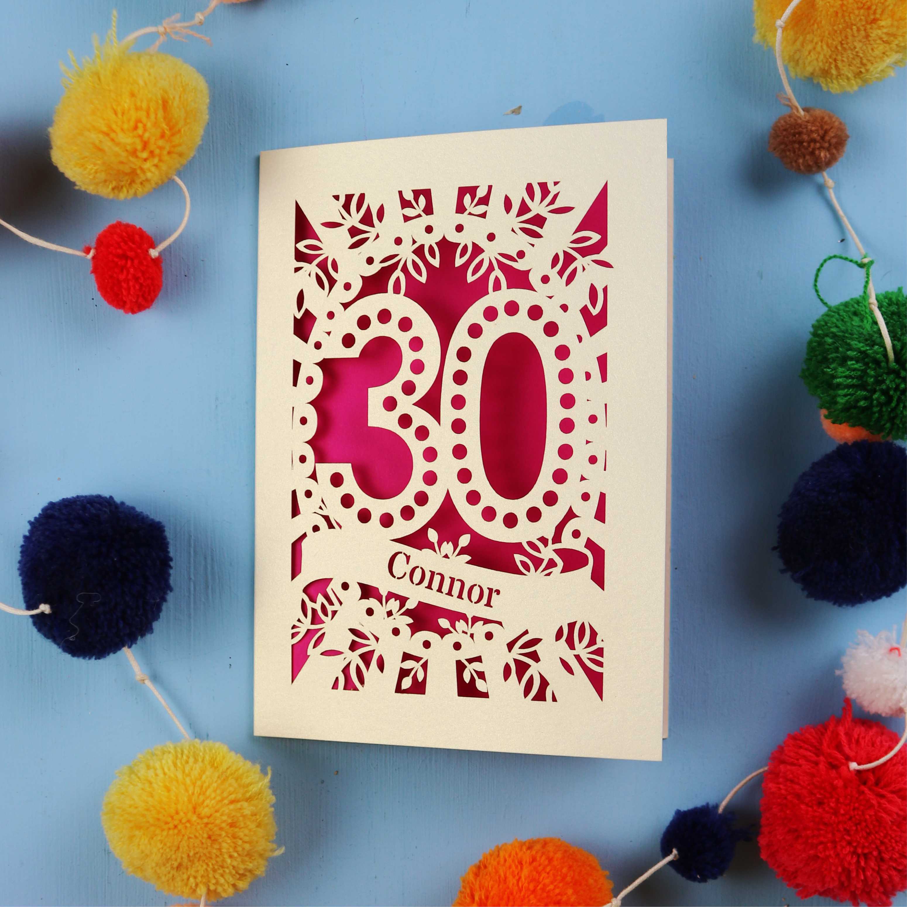 Laser cut 30th birthday card with '30 Connor' on a blue background with colourful pom-poms