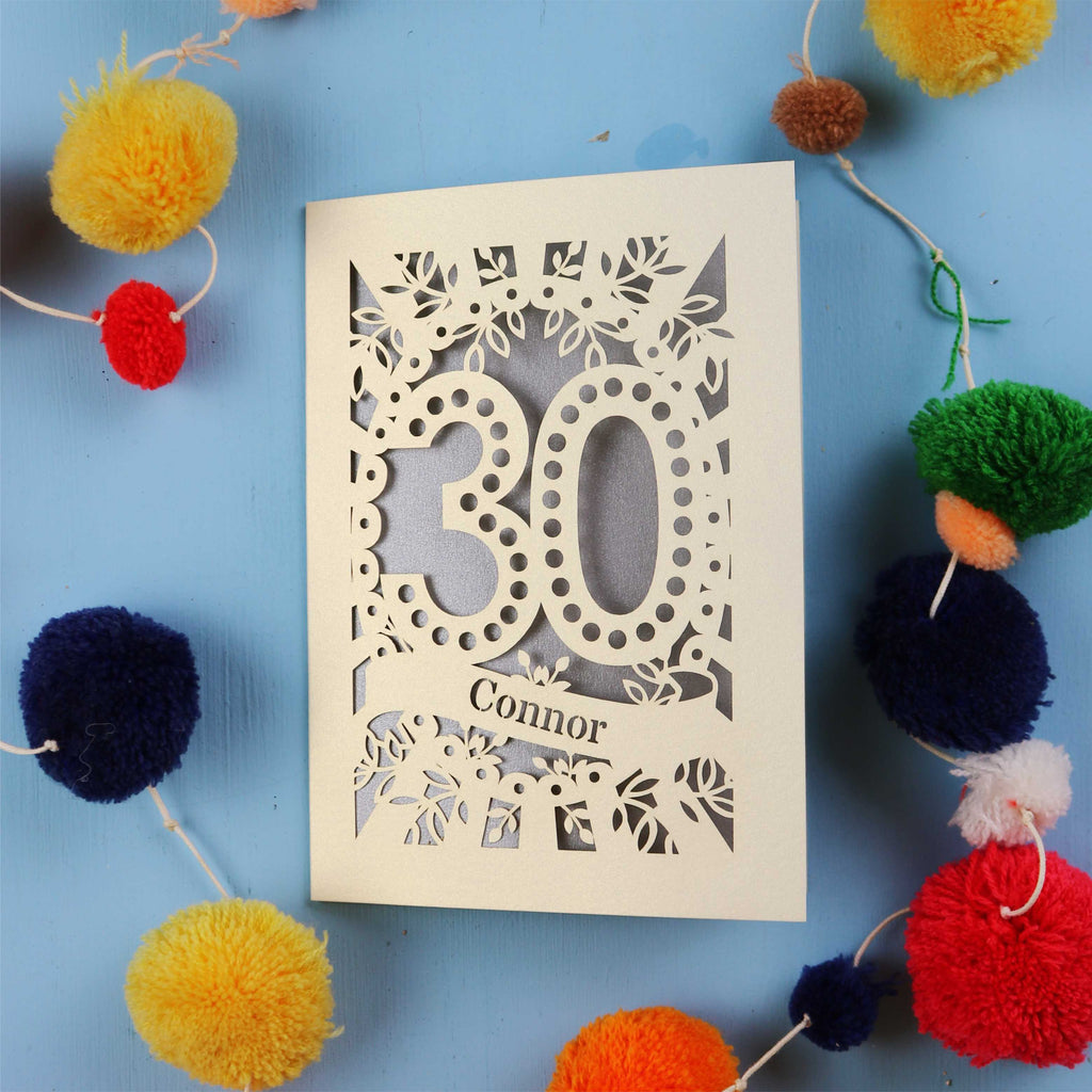 Laser cut 30th birthday card with '30 Connor' on a blue background with colourful pom-poms