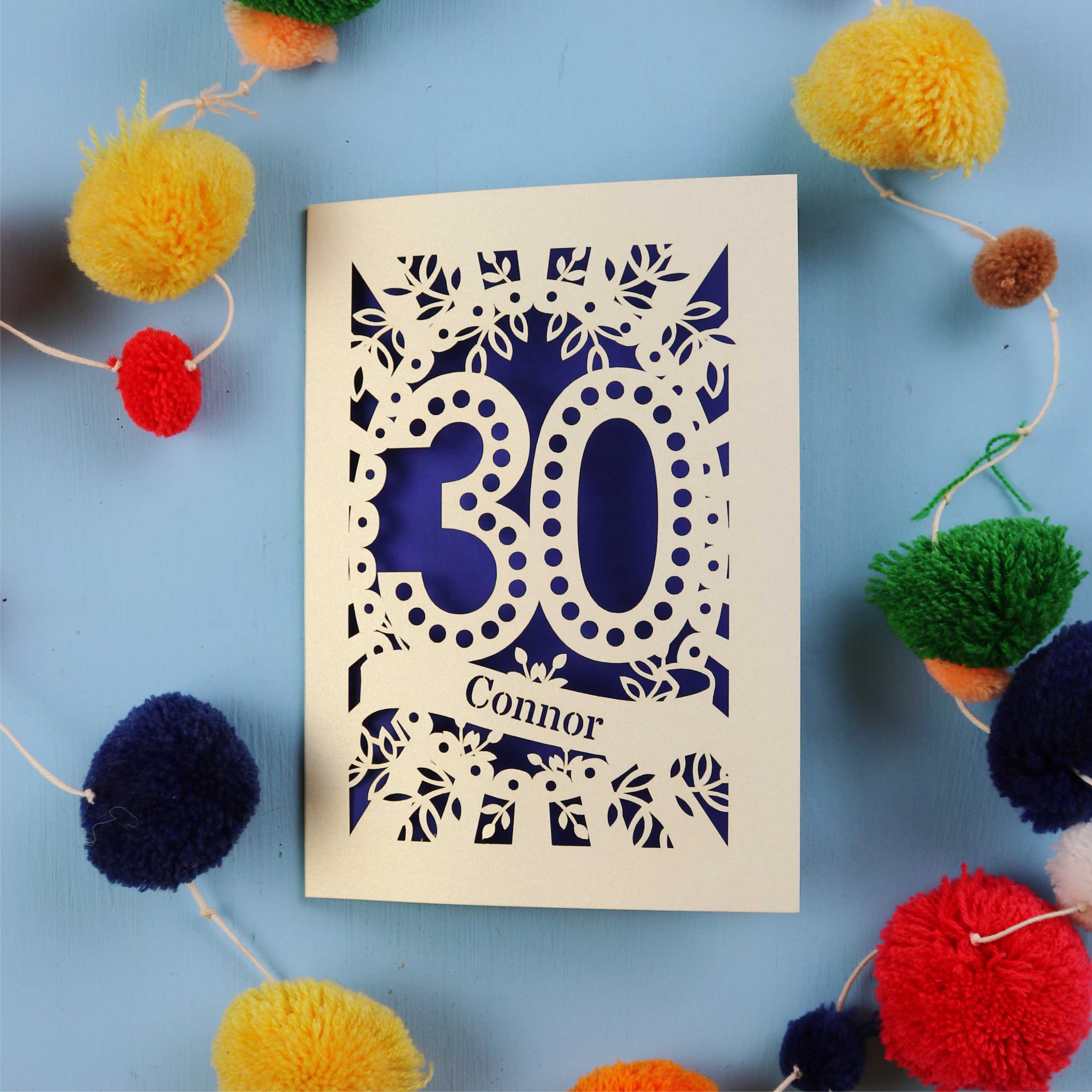 Laser cut 30th birthday card with '30 Connor' on a blue background with colourful pom-poms