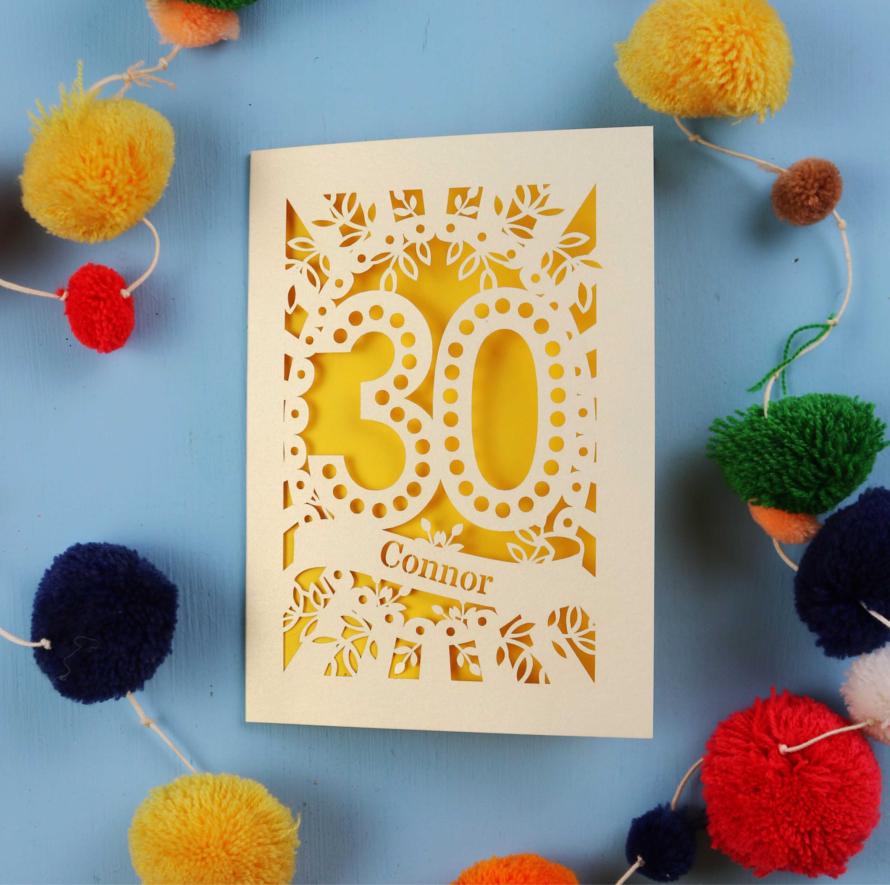 Laser cut 30th birthday card with '30 Connor' on a blue background with colourful pom-poms