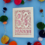 Decorative paper cut out 30th birthday card with '30 Danny' on a blue background with colourful pom-poms.