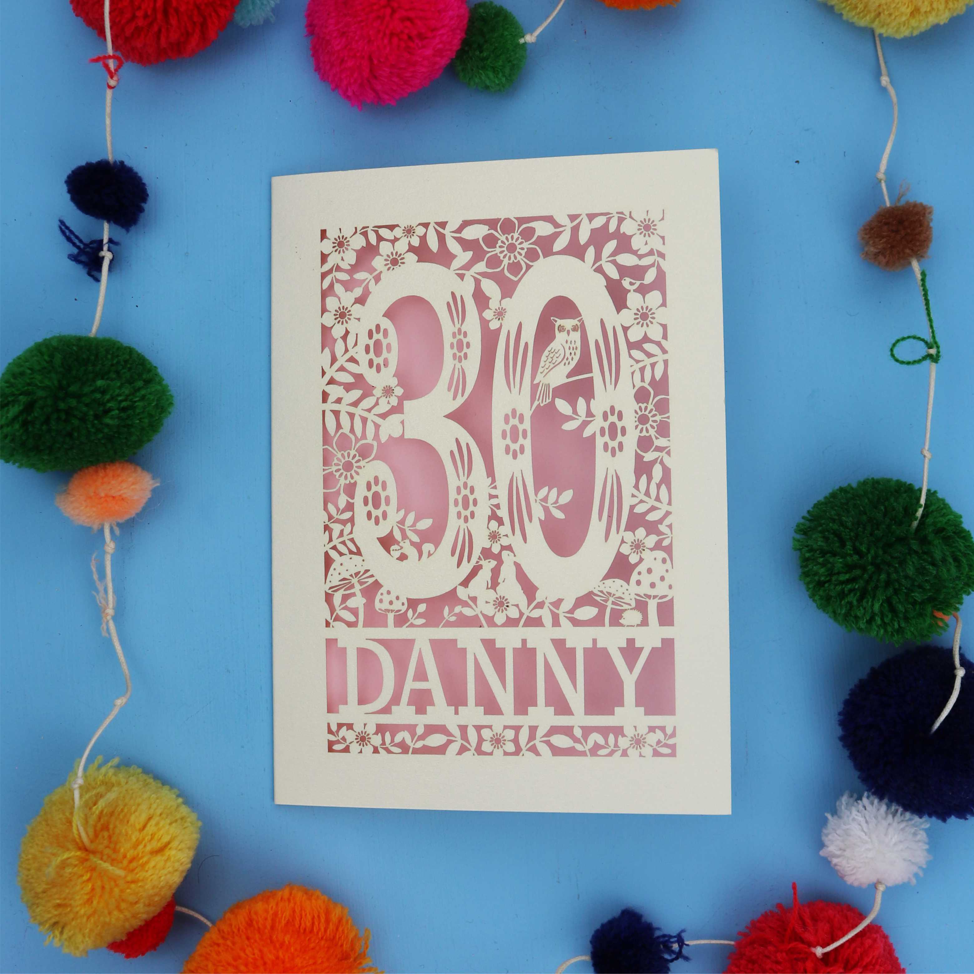 Decorative paper cut out 30th birthday card with '30 Danny' on a blue background with colourful pom-poms.