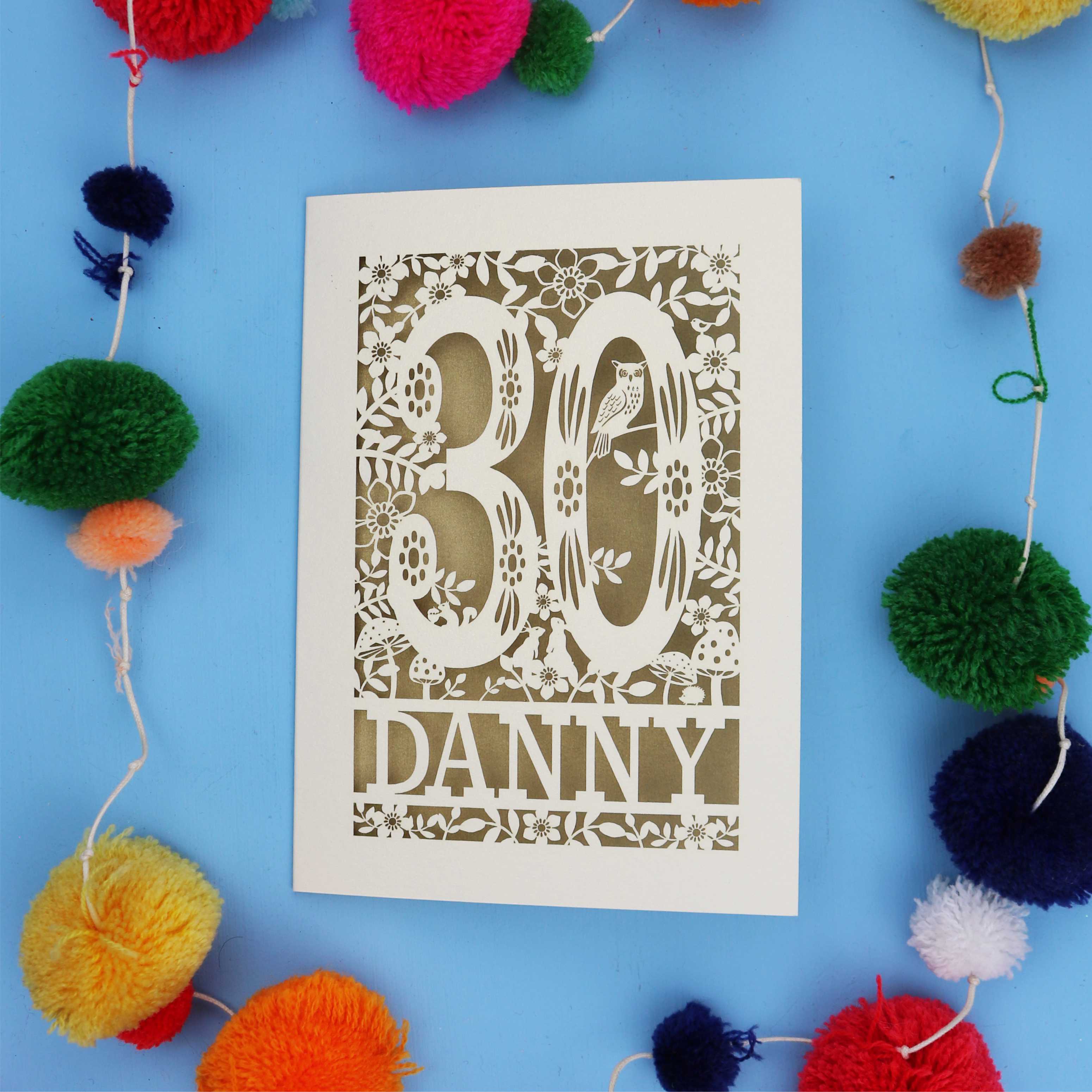 Decorative paper cut out 30th birthday card with '30 Danny' on a blue background with colourful pom-poms.