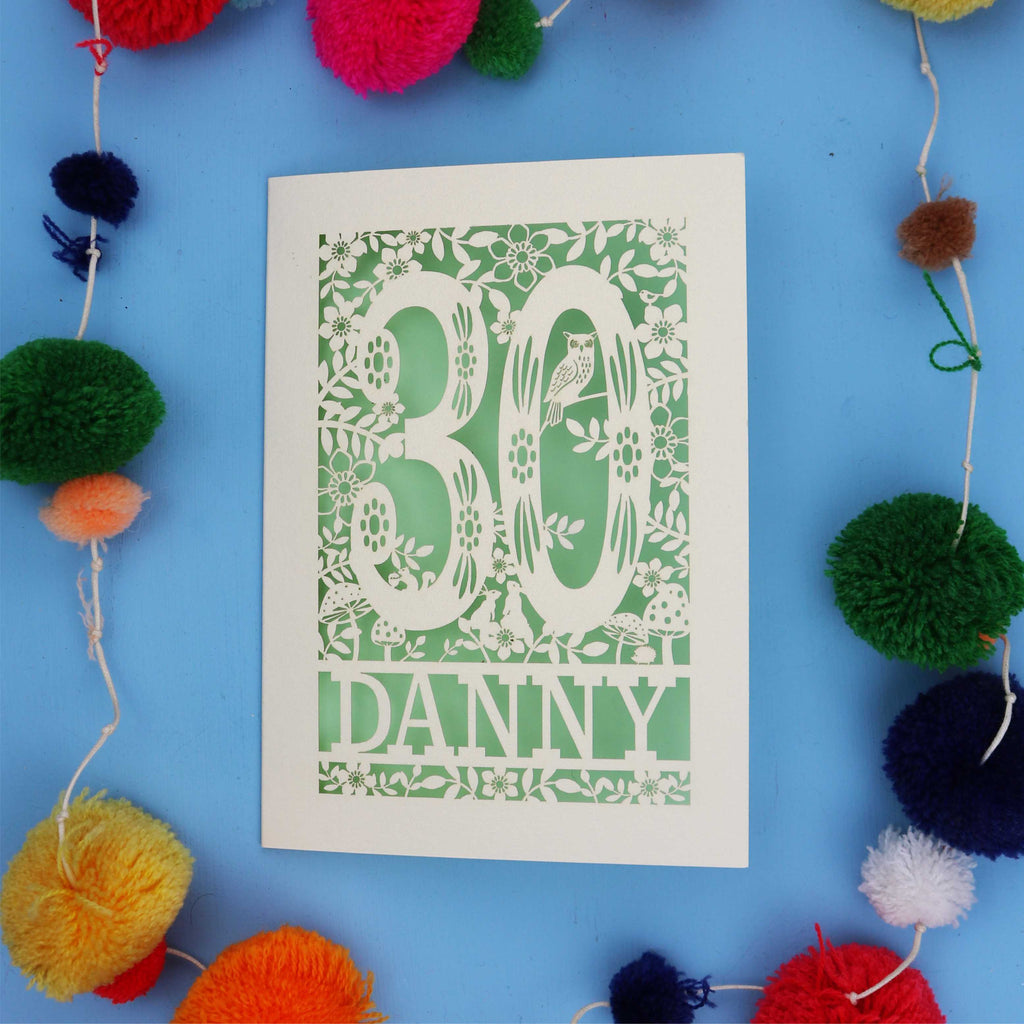 Decorative paper cut out 30th birthday card with '30 Danny' on a blue background with colourful pom-poms.