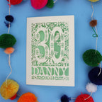 Decorative paper cut out 30th birthday card with '30 Danny' on a blue background with colourful pom-poms.