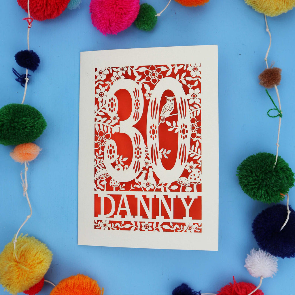 Decorative paper cut out 30th birthday card with '30 Danny' on a blue background with colourful pom-poms.