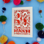 Decorative paper cut out 30th birthday card with '30 Danny' on a blue background with colourful pom-poms.