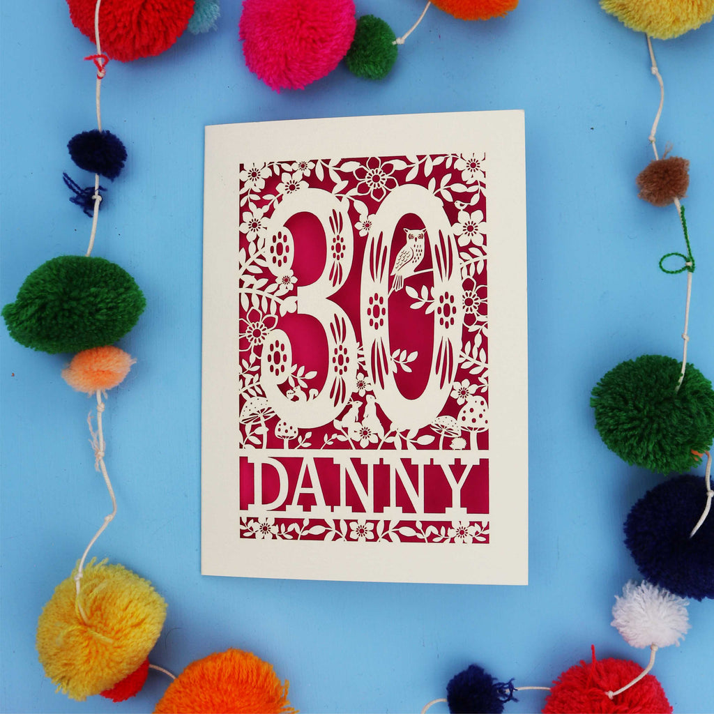 Decorative paper cut out 30th birthday card with '30 Danny' on a blue background with colourful pom-poms.