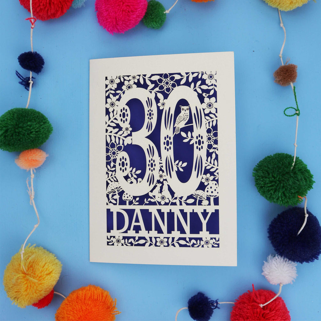 Decorative paper cut out 30th birthday card with '30 Danny' on a blue background with colourful pom-poms.