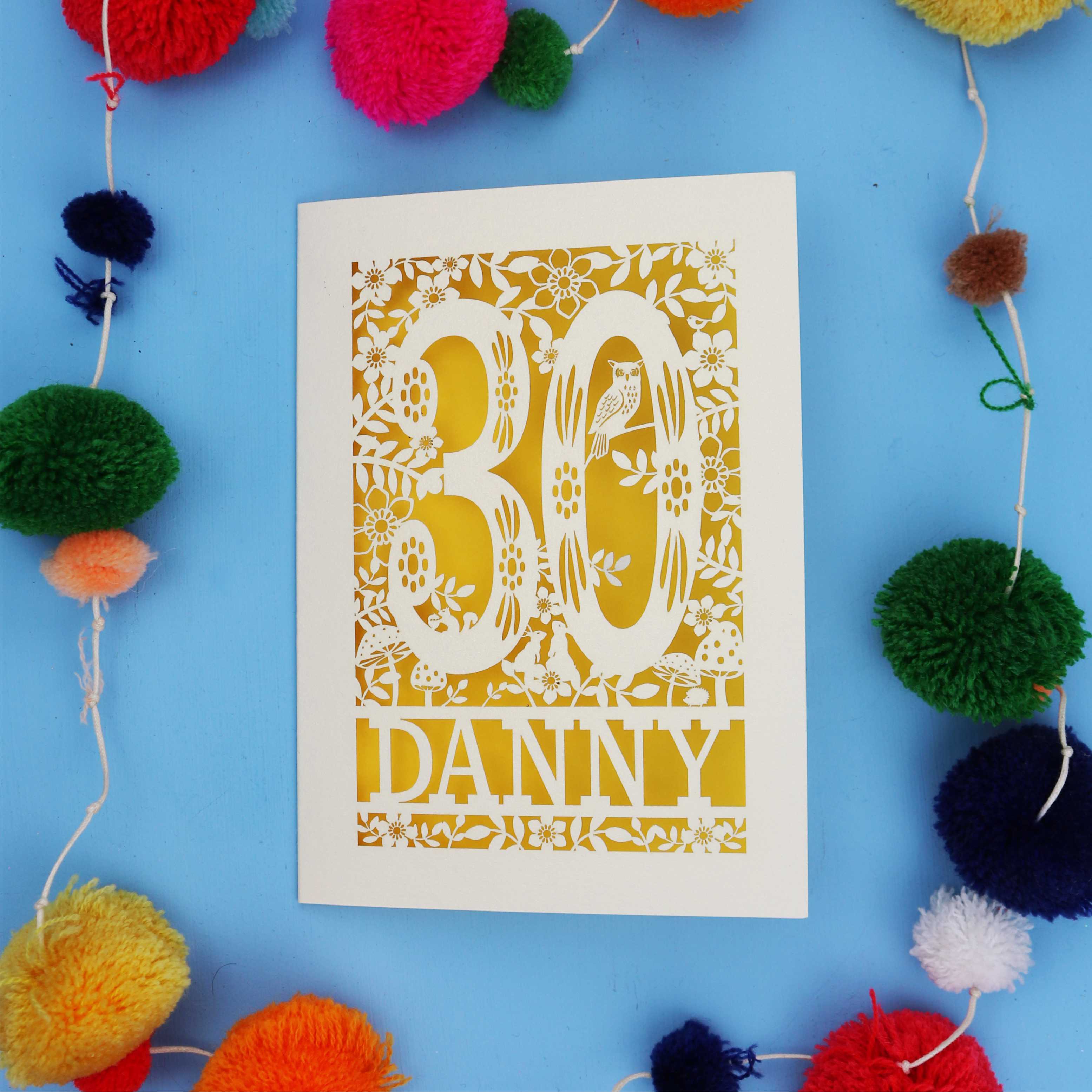 Decorative paper cut out 30th birthday card with '30 Danny' on a blue background with colourful pom-poms.