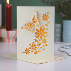 Mum card with butterfly and floral design on a table with a candle and plant in the background