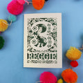Decorative paper cut out 3rd birthday card with floral patterns and 'REGGIE' text on a blue background with colourful pom-poms.