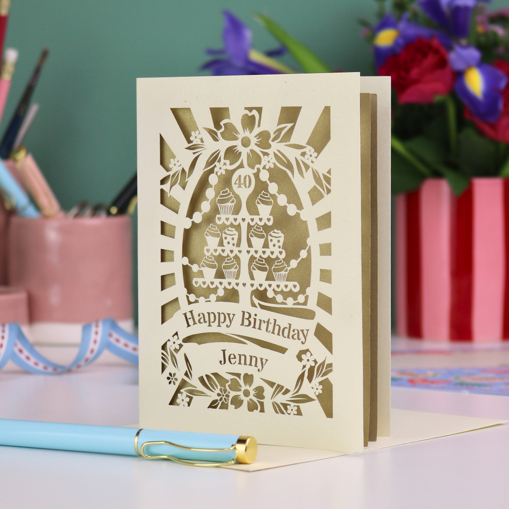 Personalised 40th birthday card with decorative cut-out cupcakes on a cake stand design on a desk with stationery items.
