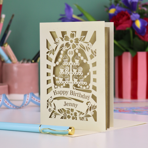 Personalised 40th birthday card with decorative cut-out cupcakes on a cake stand design on a desk with stationery items.