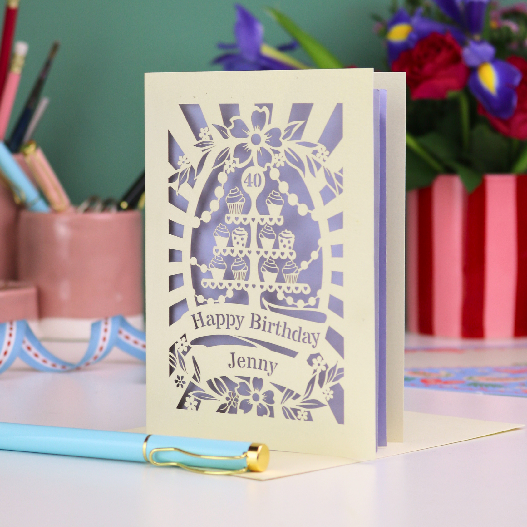 Personalized 40th birthday card with decorative cut-out cupcakes on a cake stand design on a desk with stationery items.