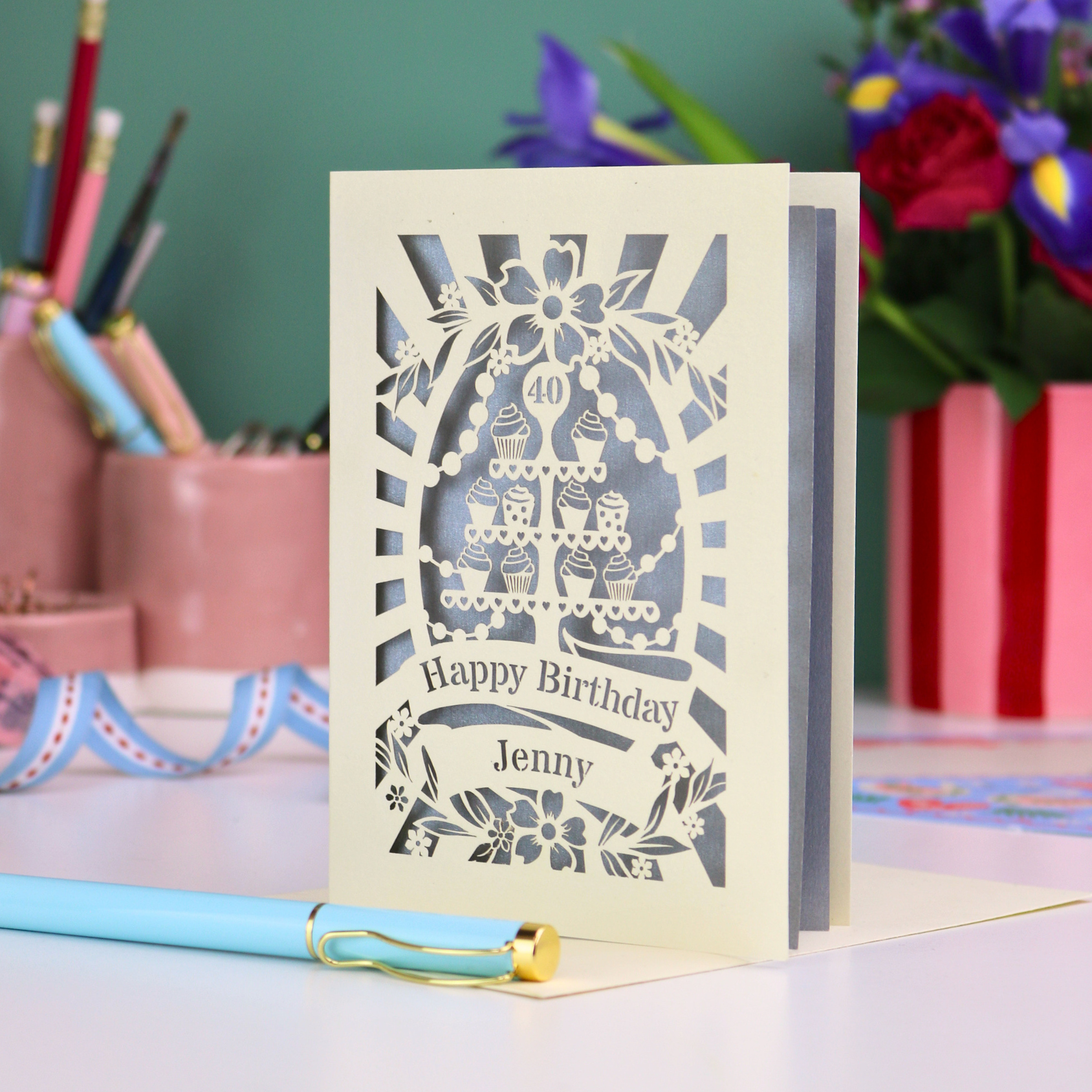 Personalized 40th birthday card with decorative cut-out cupcakes on a cake stand design on a desk with stationery items.