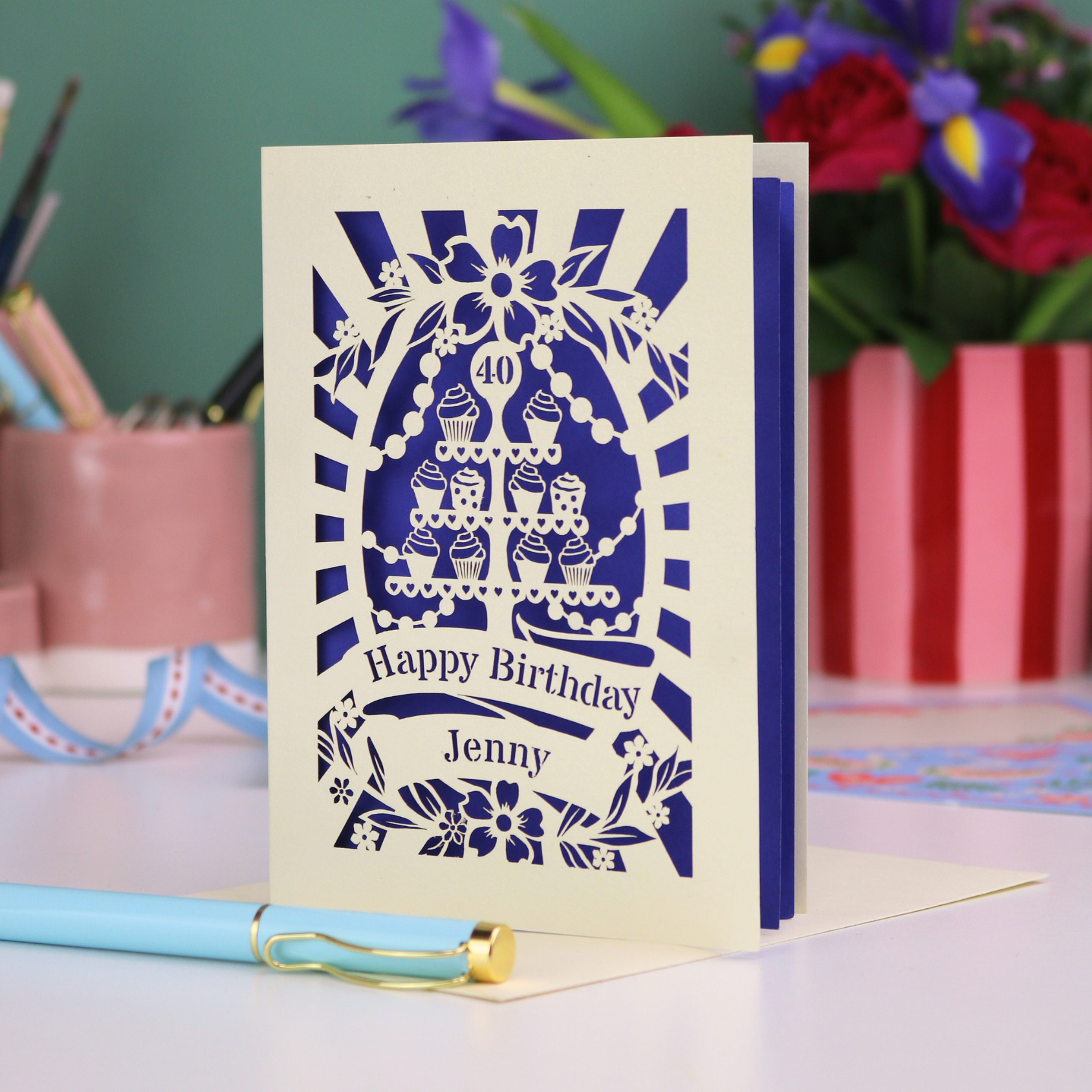 Personalized 40th birthday card with decorative cut-out cupcakes on a cake stand design on a desk with stationery items.