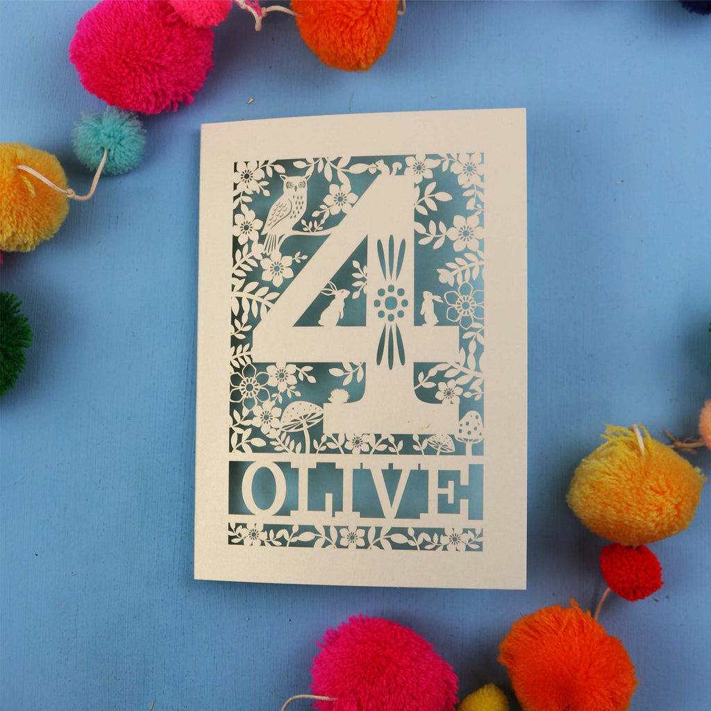 Woodland personalised 4th birthday card with number '4' and 'OLIVE' text on a blue background with colourful pom-poms.