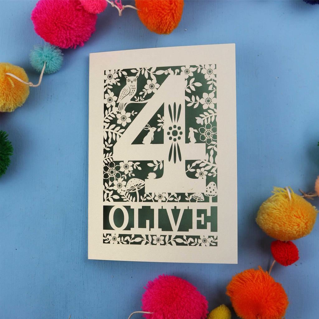 Woodland 4th birthday card with number '4' and 'OLIVE' text on a blue background with colourful pom-poms.