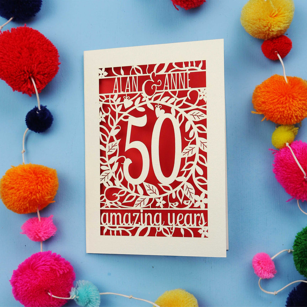 50th Anniversary Card with '50 amazing years' design on a blue background with colourful pom-poms.