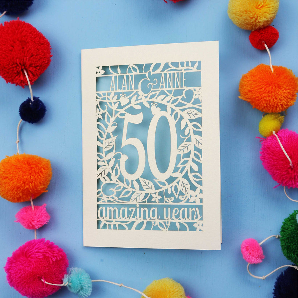 Golden wedding Anniversary Card with '50 amazing years' design on a blue background with colourful pom-poms.