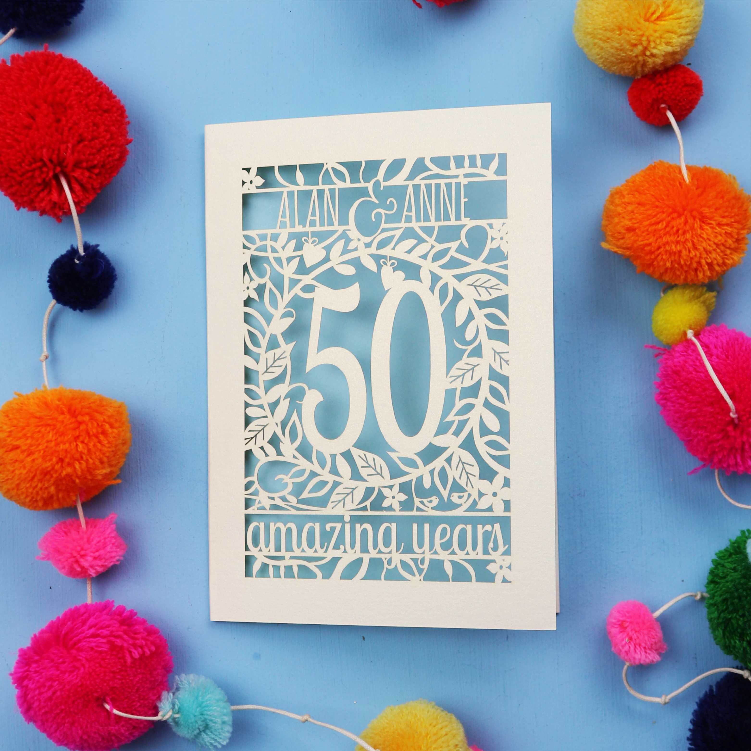 Golden wedding Anniversary Card with '50 amazing years' design on a blue background with colourful pom-poms.