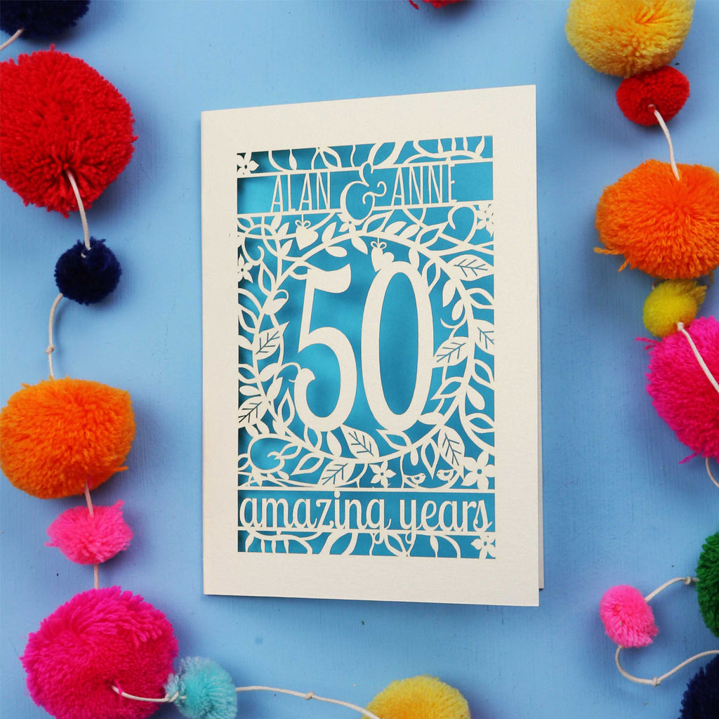 50th Anniversary Card with '50 amazing years' design on a blue background with colourful pom-poms.