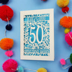50th Anniversary Card with '50 amazing years' design on a blue background with colourful pom-poms.