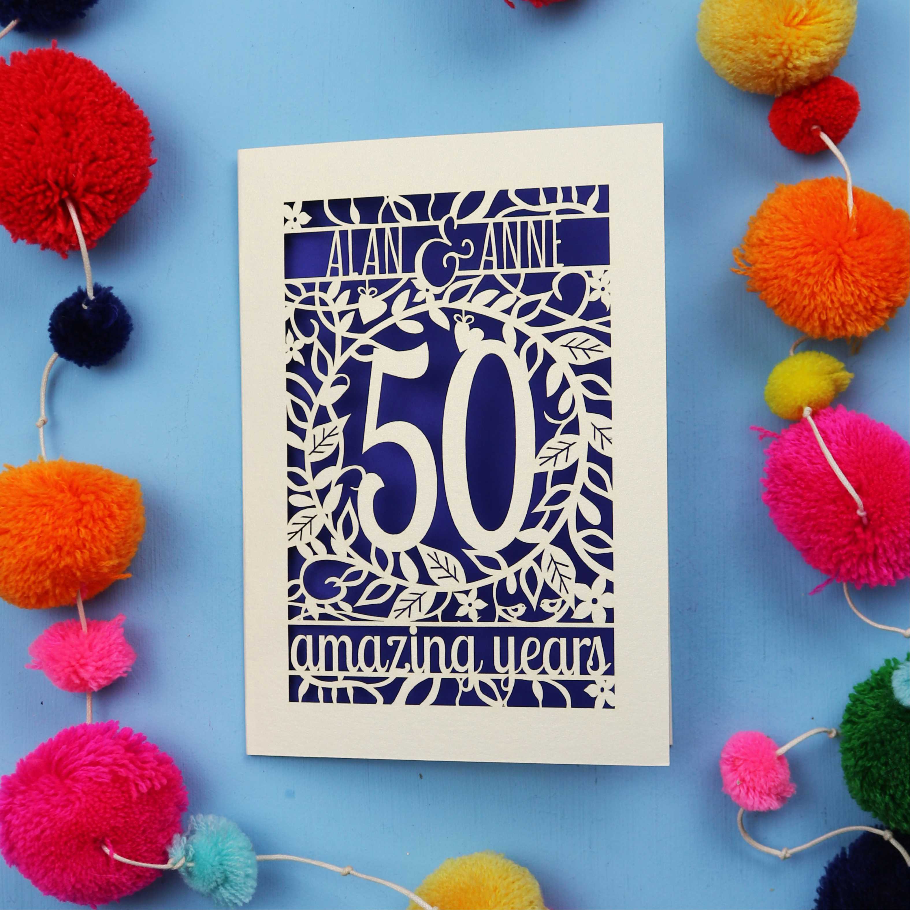 50th Anniversary Card with '50 amazing years' design on a blue background with colourful pom-poms.