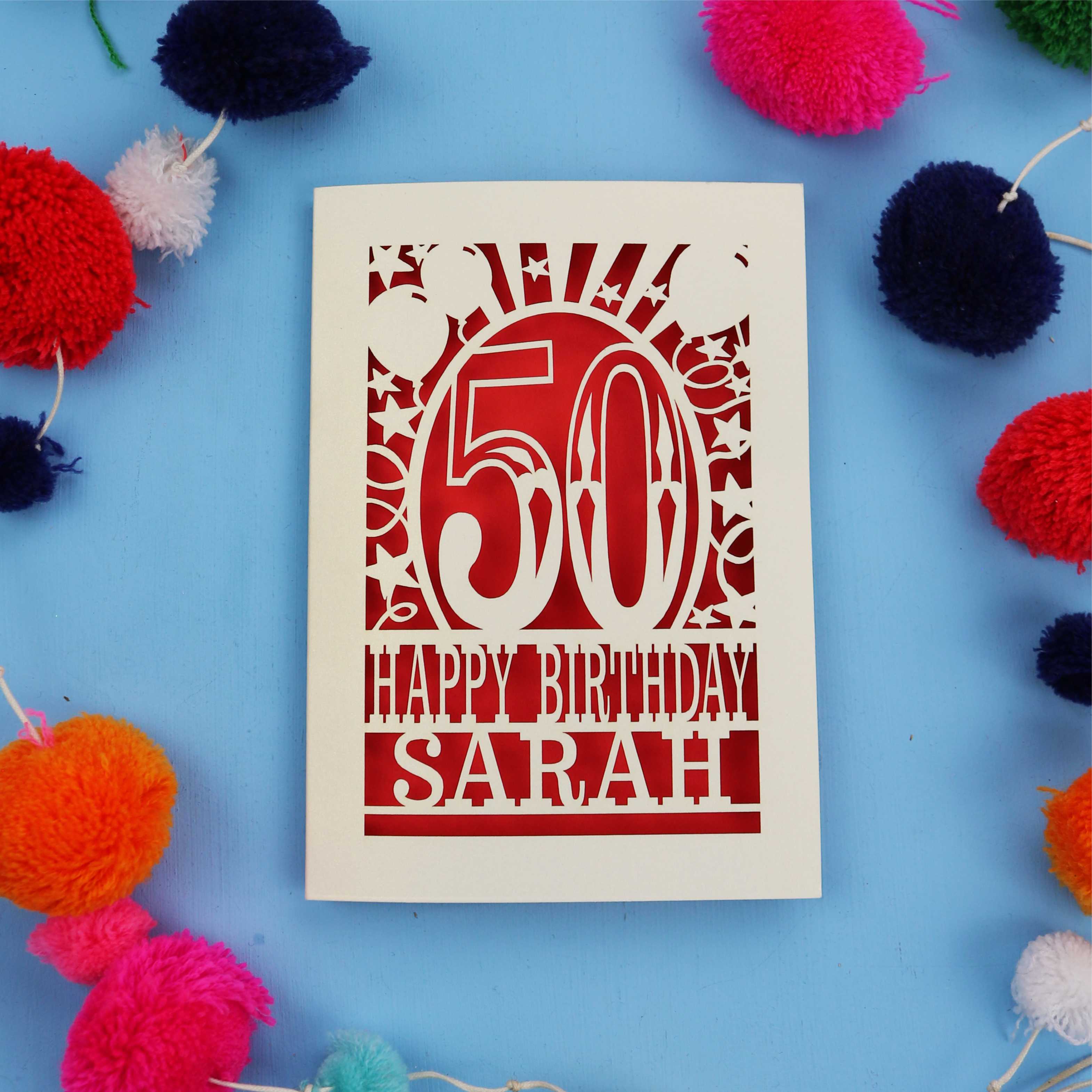Laser cut Happy 50th birthday card with colourful pom-poms on a blue background