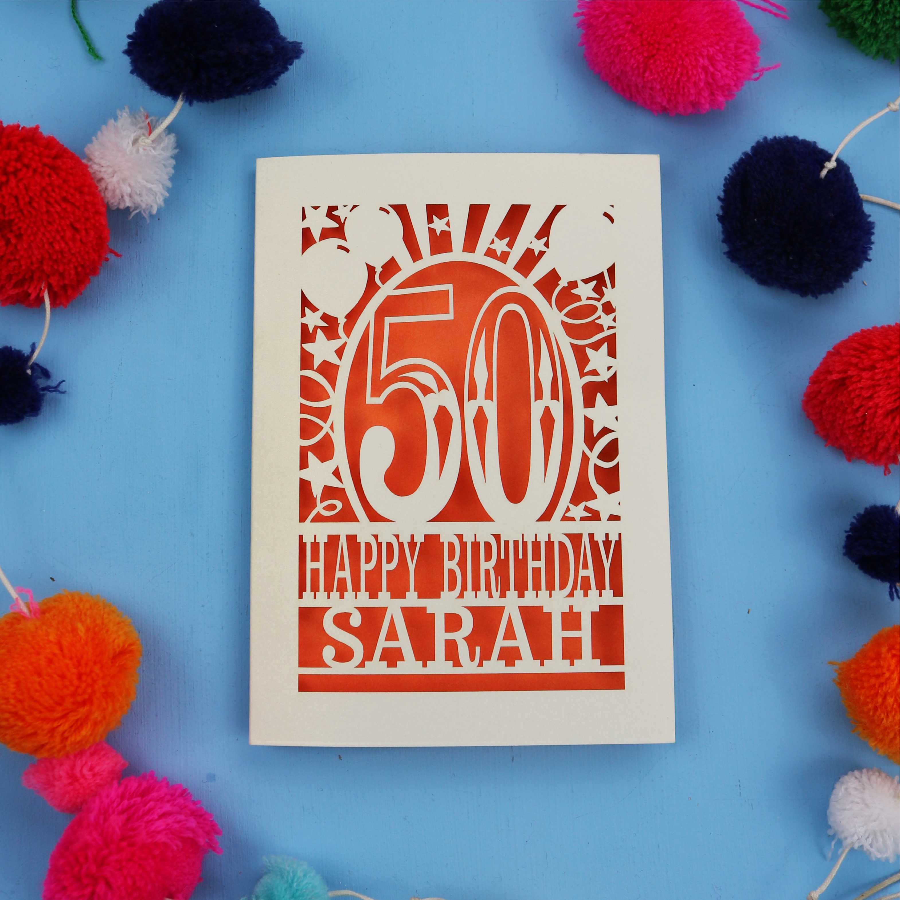 Laser cut Happy 50th birthday card with colourful pom-poms on a blue background