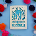 Paper cut Happy 50th birthday card with colourful pom-poms on a blue background