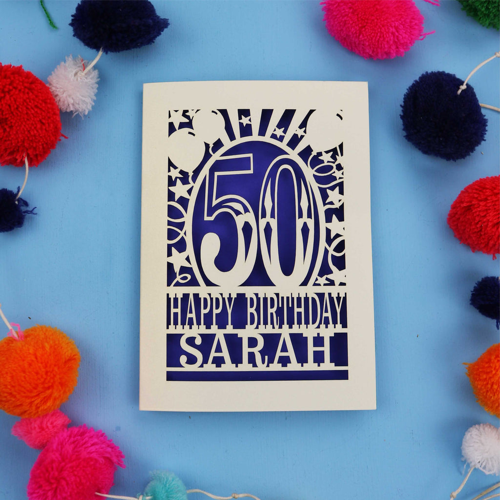Laser cut Happy 50th birthday card with colourful pom-poms on a blue background