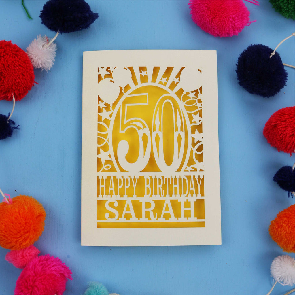 Laser cut Happy 50th birthday card with colourful pom-poms on a blue background