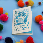 A 50th birthday Card with '50' and 'Lesley' on a blue background with colourful pom-poms