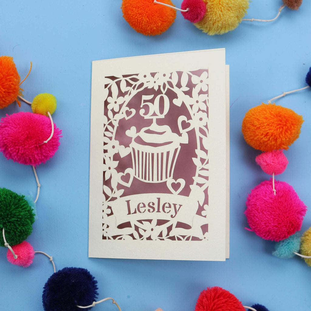 A 50th birthday Card with '50' and 'Lesley' on a blue background with colourful pom-poms