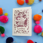 A 50th birthday Card with '50' and 'Lesley' on a blue background with colourful pom-poms