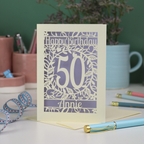 A 50th birthday card, personalised with the number 50 and the name Annie, on a white desk with stationery items. 