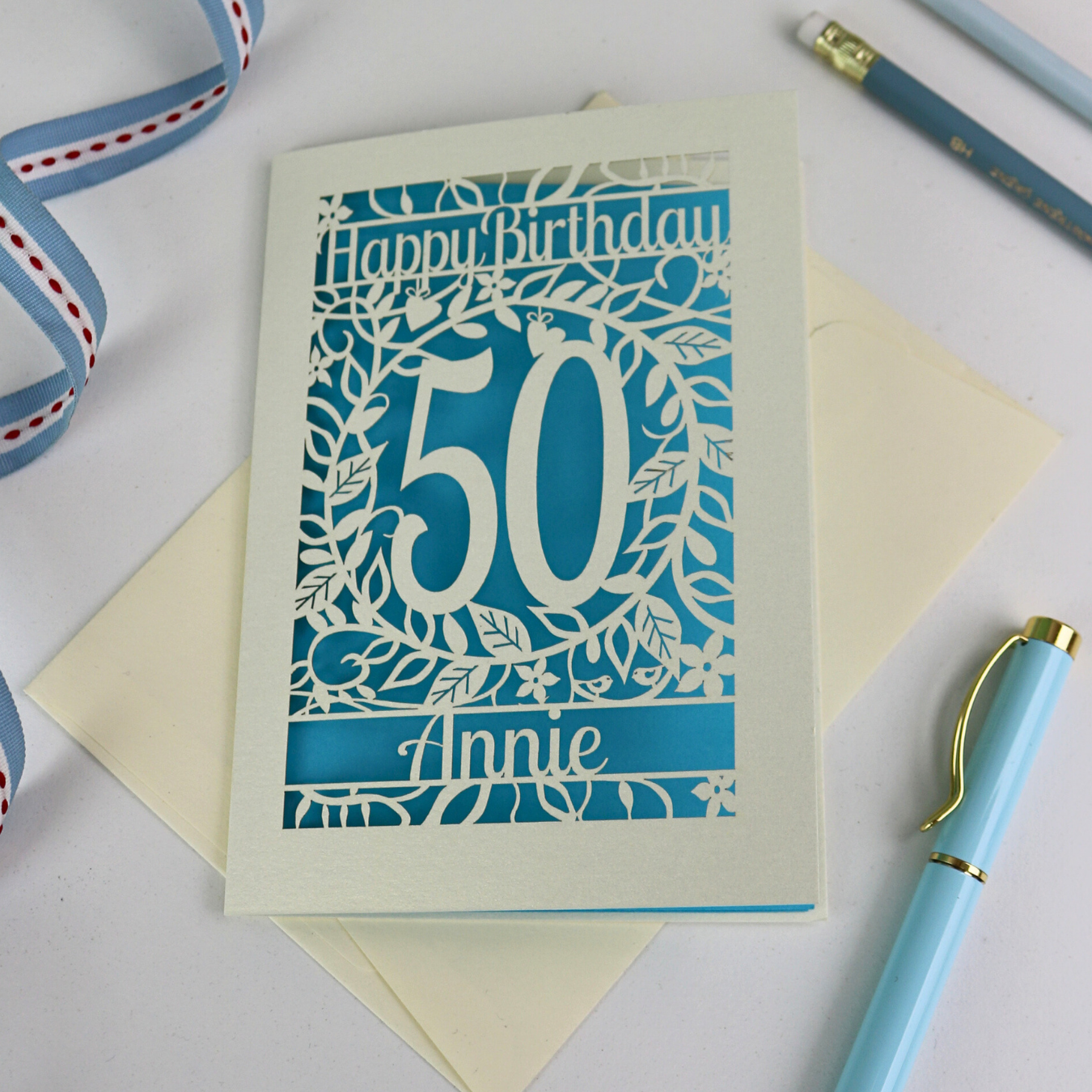 A laser cut 50th birthday card, personalised with the number 50 and the name Annie, on a white desk.